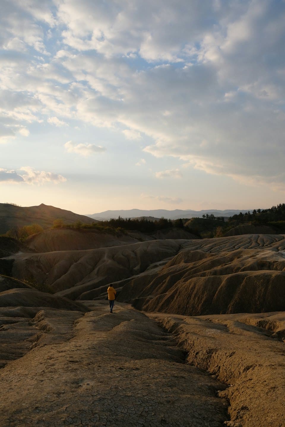 Person in yellow jacket walks through dry badlands at sunrise.